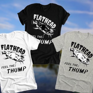 May include: Three t-shirts featuring a black and white graphic of a catfish with the text "Flathead Feel the Thump". The shirts are white, black, and heather grey.
