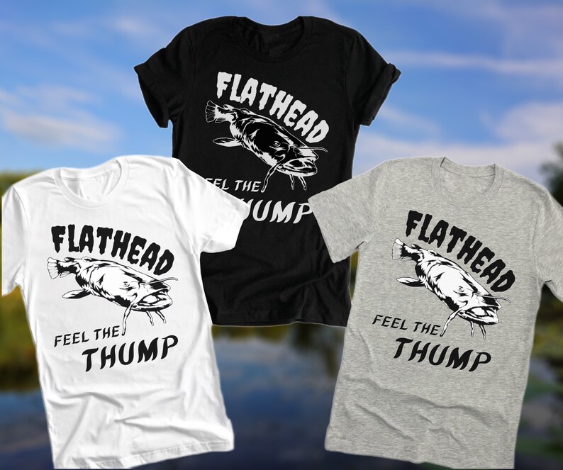 May include: Three t-shirts featuring a black and white graphic of a catfish with the text "Flathead Feel the Thump". The shirts are white, black, and heather grey.
