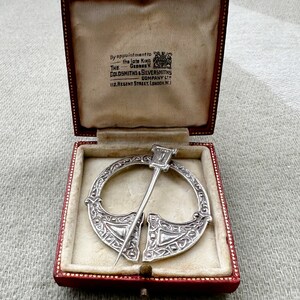 Könnte beinhalten: Eine silberne keltische Brosche in einer roten Samtbox. Die Box trägt ein Etikett mit der Aufschrift "By appointment to the late King George V The Goldsmiths & Silversmiths Company Ltd 112 Regent Street, London, W.1."