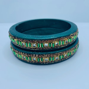 May include: Two green bangles with gold and green embellishments. The bangles are decorated with small, clear rhinestones and green and gold stripes.