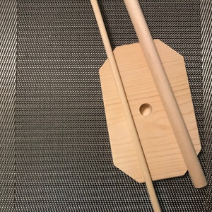 May include: A wooden base with a hole in the center and two wooden dowels. The base is light brown and the dowels are a slightly darker brown.