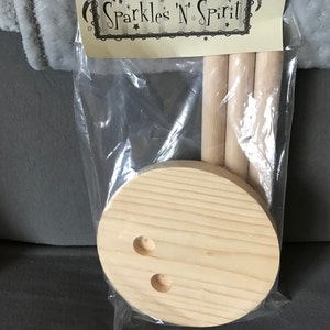 May include: A wooden craft kit with three dowels and a round wooden base with two holes. The kit is packaged in a clear plastic bag with a label that reads "Sparkles 'N' Spirit".