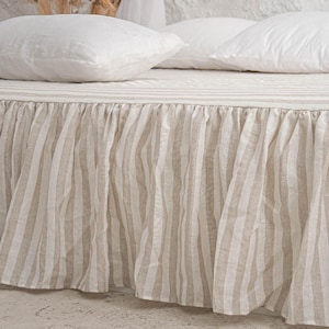 May include: A bed with a beige and white striped bed skirt and matching striped bedspread. Two white pillows rest on the bed. The bed skirt is ruffled and hangs to the floor.
