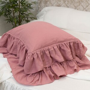 Puede incluir: Una almohada rosa polvorienta con un borde con volantes. La almohada est&aacute; hecha de una tela de lino suave y tiene un dise&ntilde;o simple y elegante.