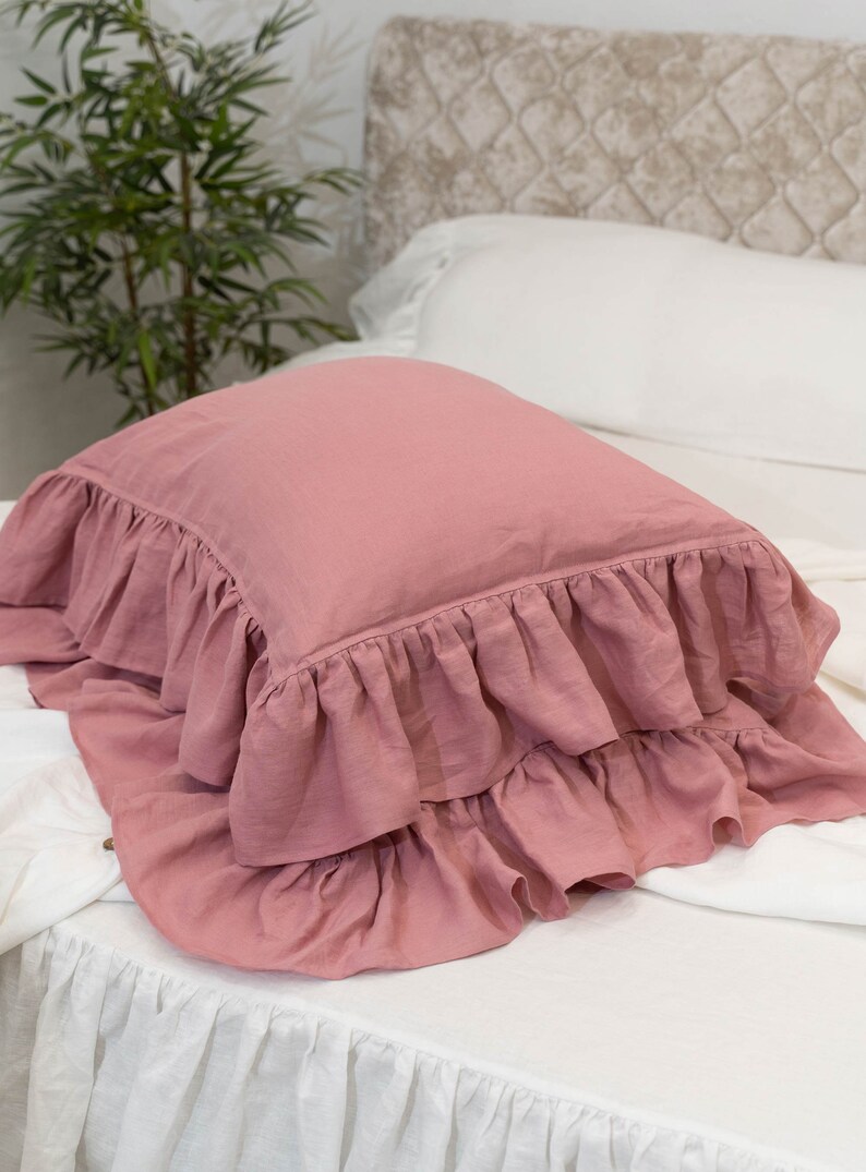 Puede incluir: Una almohada rosa polvorienta con un borde con volantes. La almohada est&aacute; hecha de una tela de lino suave y tiene un dise&ntilde;o simple y elegante.