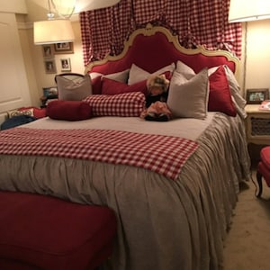 May include: A red and white checkered bedspread with a ruffled edge, a red headboard, and a white and gray pillow with a doll on top.