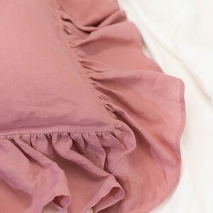 Puede incluir: Una almohada rosa polvorienta con un borde con volantes. La almohada est&aacute; hecha de una tela de lino suave.