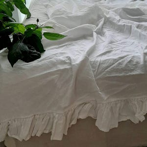 Peut inclure: Drap de lit en lin blanc avec un bord festonné. Le drap est drapé sur un lit et a un aspect naturel et détendu.