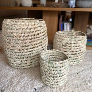 Peut inclure: Trois paniers tressés de tailles différentes. Les paniers sont faits d'un matériau naturel de couleur claire, peut-être de la paille ou des roseaux. Ils ont une forme cylindrique avec une surface légèrement texturée et sont disposés sur un tapis blanc.