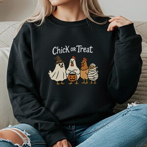 May include: Black sweatshirt featuring the phrase "Chick or Treat" and a graphic of four chickens in Halloween costumes. The chickens are dressed as a ghost, a mummy, and a witch, with one holding a pumpkin.