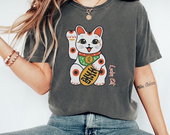 May include: Dark grey t-shirt with a cartoon Lucky Cat design. The cat is white with red and black accents, holding a gold coin. The shirt has the text "Lucky Cat" in red and Japanese characters.