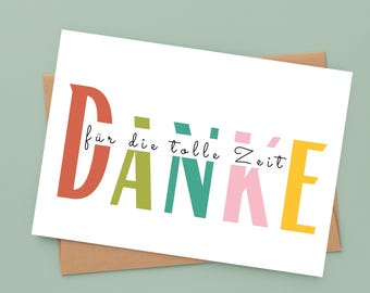 May include: A white greeting card with the word "DANKE" in large, colorful letters. The card also includes the phrase "für die tolle Zeit" in a smaller font. The card is on a brown envelope, set against a light green background.