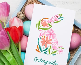May include: A white card with a watercolor illustration of a pink and green bunny rabbit made of flowers. The card has the text "Ostergrüße" in green.