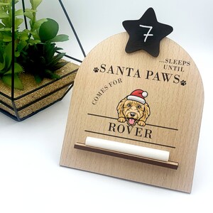 May include: Wooden countdown calendar with a black star and a chalk number 7. The calendar says "...sleeps until Santa Paws comes for Rover".