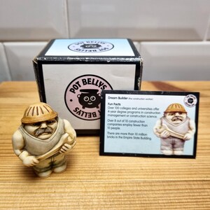 May include: A small, off-white figurine of a construction worker holding a wrench, with a mustache and a hard hat. The figurine is next to a box with the Pot Belly's logo and a card with fun facts about construction. The figurine is approximately 7.6 cm tall.