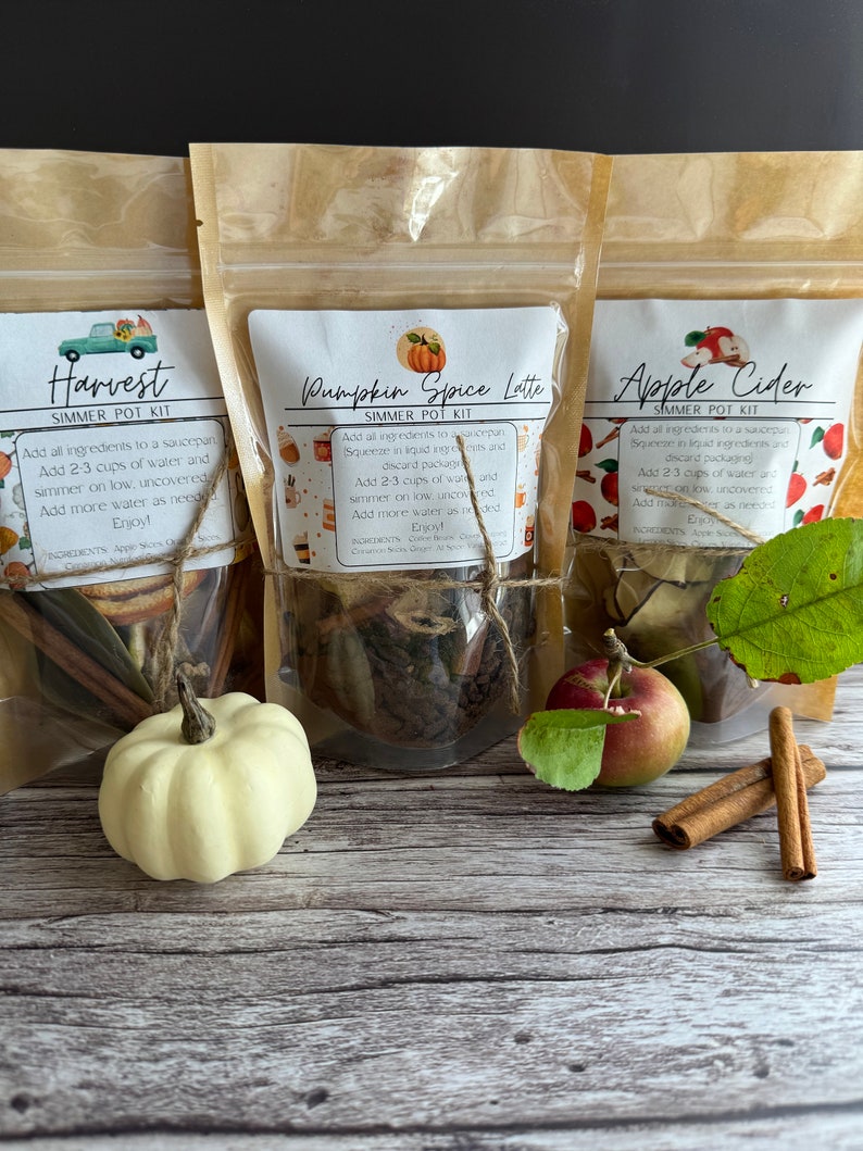 May include: Three brown paper bags with labels for simmer pot kits. The labels are for Harvest, Pumpkin Spice Latte, and Apple Cider. Each bag contains a variety of ingredients, including cinnamon sticks, dried fruit, and spices.