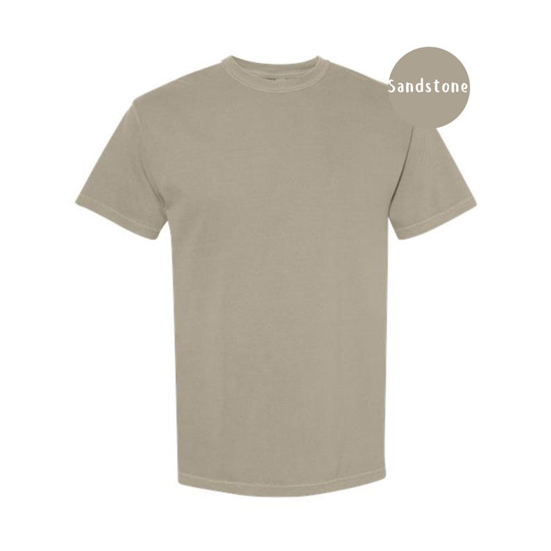 Pode incluir: Uma t-shirt de manga curta com gola redonda numa cor bege arenito s&oacute;lida. A pe&ccedil;a apresenta um corte padr&atilde;o com gola canelada e mangas com bainha. Um gr&aacute;fico circular no canto superior direito cont&eacute;m o texto Sandstone.
