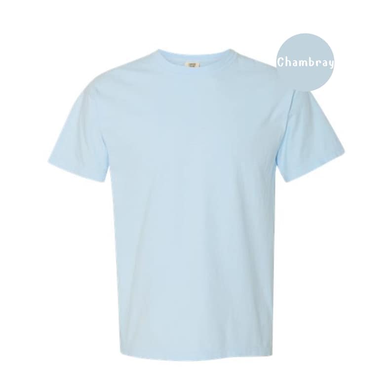Pode incluir: Uma t-shirt de manga curta com gola redonda numa cor azul-claro s&oacute;lida. A pe&ccedil;a apresenta um corte padr&atilde;o com gola canelada e mangas curtas. Um gr&aacute;fico circular azul-claro no canto superior direito cont&eacute;m o texto Chambray.