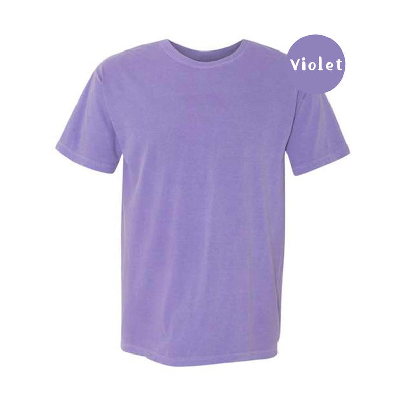 Pode incluir: Uma t-shirt de manga curta em cor violeta s&oacute;lida com decote redondo. Um gr&aacute;fico circular roxo no canto superior direito cont&eacute;m o texto branco Violet. A pe&ccedil;a apresenta um corte padr&atilde;o com uma bainha reta.