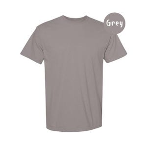 Pode incluir: Uma t-shirt cinzenta de manga curta com decote redondo. A pe&ccedil;a apresenta uma cor uniforme em todo o tecido. Um emblema circular cinzento no canto superior direito cont&eacute;m o texto branco Grey, indicando a cor da pe&ccedil;a de vestu&aacute;rio.
