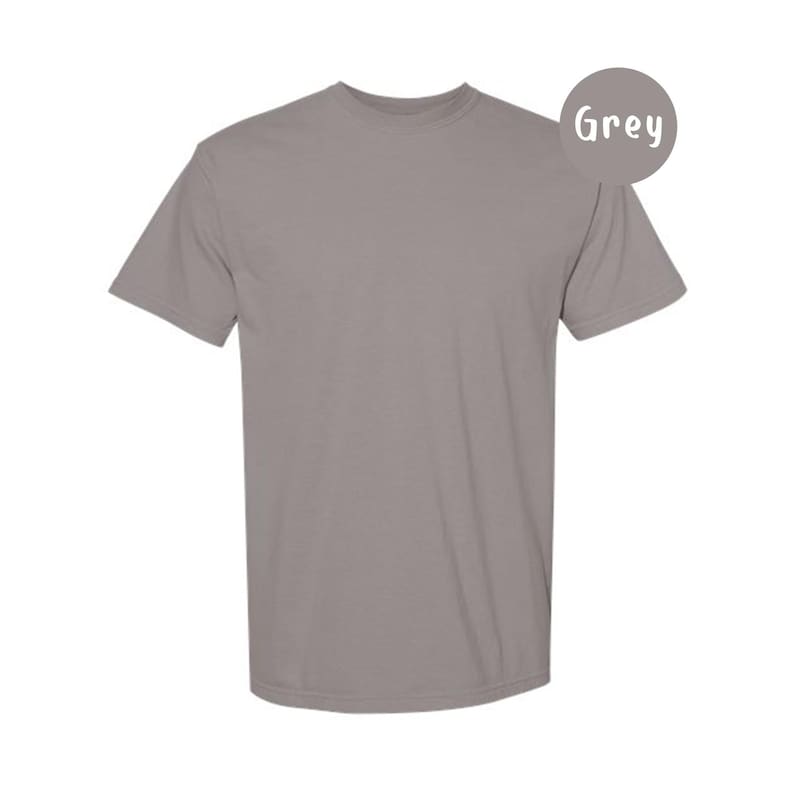 Pode incluir: Uma t-shirt cinzenta de manga curta com decote redondo. A pe&ccedil;a apresenta uma cor uniforme em todo o tecido. Um emblema circular cinzento no canto superior direito cont&eacute;m o texto branco Grey, indicando a cor da pe&ccedil;a de vestu&aacute;rio.