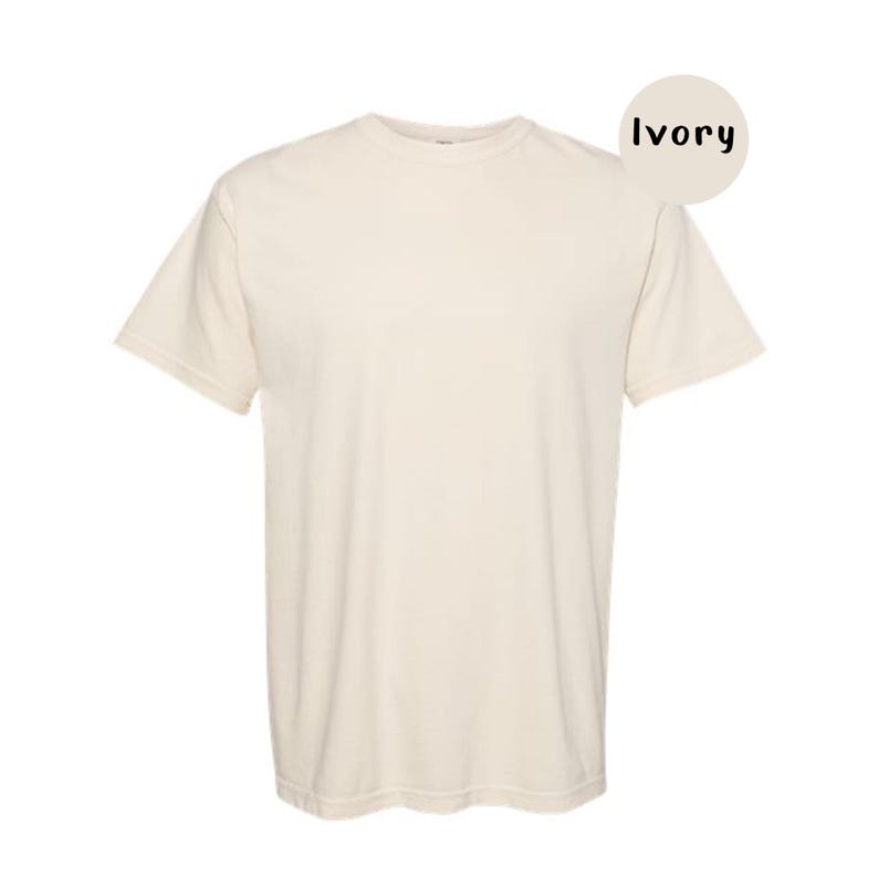 Pode incluir: Uma t-shirt de manga curta em cor marfim s&oacute;lida. A pe&ccedil;a apresenta um decote redondo e um corte padr&atilde;o. Um gr&aacute;fico circular no canto superior direito cont&eacute;m o texto Ivory, indicando a cor espec&iacute;fica do tecido apresentado na imagem.