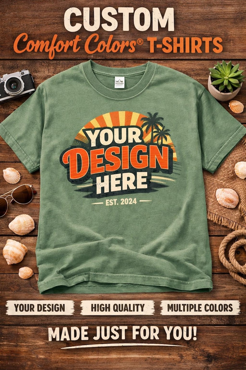 K&ouml;nnte beinhalten: Ein salbeigr&uuml;nes Comfort Colors T-Shirt mit einem Grafikdesign mit der Aufschrift "YOUR DESIGN HERE" in Orange und Wei&szlig;, mit Sonnenuntergang und Palmen. Der Text "EST. 2024" steht darunter. Das T-Shirt liegt auf einem Holzgrund.