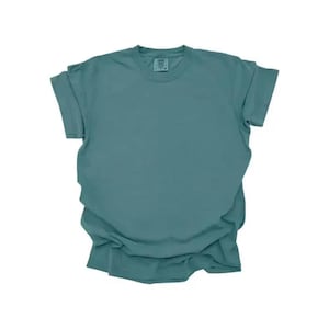 K&ouml;nnte beinhalten: Ein einfarbiges, teal-farbenes T-Shirt mit kurzen &Auml;rmeln. Das Shirt besteht aus einem weichen Material und hat einen Rundhalsausschnitt. Die &Auml;rmel sind hochgekrempelt. Das Shirt liegt flach auf einer wei&szlig;en Oberfl&auml;che.