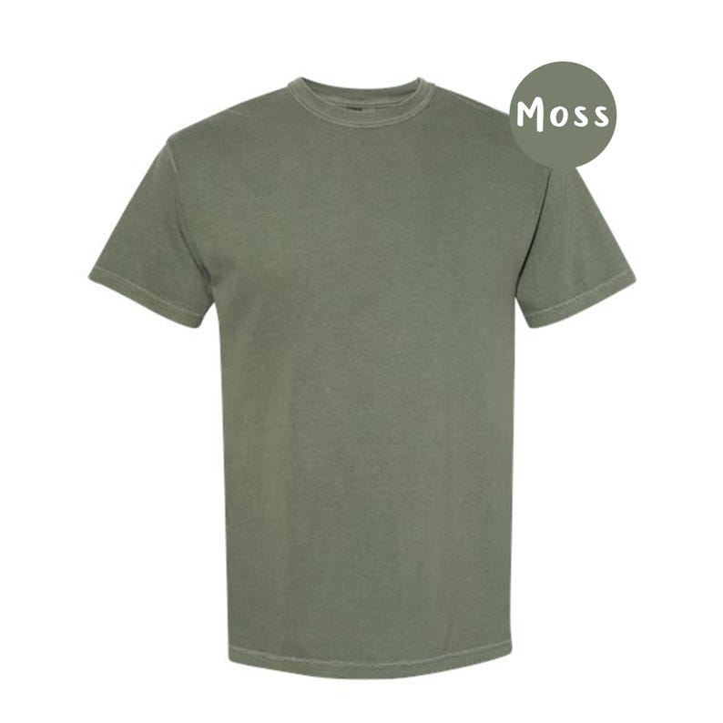 Pode incluir: Uma t-shirt de manga curta com gola redonda em cor verde musgo s&oacute;lida. O tecido tem um aspeto ligeiramente desbotado e vintage. Um emblema circular no canto superior direito exibe o texto Moss em letras mai&uacute;sculas brancas.