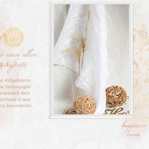 Pu&ograve; includere: Un foglio di carta velina bianca con una corona dorata e testo che recita "Per un aspetto nobile, la carta velina fine inclusa trasforma il tuo regalo in qualcosa di speciale!" La carta velina &egrave; su uno sfondo bianco con una texture dorata. Ci sono tre sfere intrecciate nell'immagine.