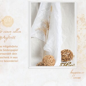 May include: A white tissue paper with a crown graphic and the text "For a noble appearance, the included tissue paper transforms your gift into something special!"  The tissue paper is draped over a white surface with two brown wicker balls and a dried grass stalk.