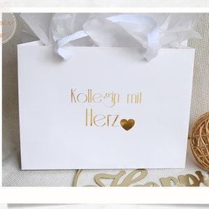 Pu&ograve; includere: Busta regalo bianca con scritta dorata "Kolleg*in mit Herz" e un cuore dorato.