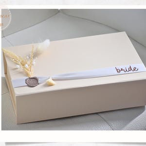 Lussuosa scatola magnetica personalizzata in beige chiaro con nastro di raso, nappa e fiori secchi. Scatola regalo per matrimoni, battesimi, nascite e compleanni.