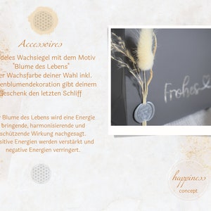 May include: A gray box with a wax seal and a dried flower arrangement. The box has the text "Frohes &" written on it. The wax seal has a flower design. The dried flower arrangement is a white fluffy flower with brown stems. The box is on a white surface. The text "happiness concept" is on a clear circle on the bottom right of the image.