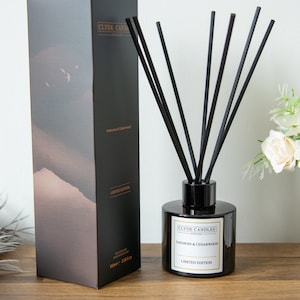 May include: A black and gold diffuser bottle with black reeds and a label that reads "Clyde Candles, Scotland, Oakmoss & Cedarwood, Limited Edition".