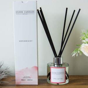 May include: White Rose & Lily Reed Diffuser by Clyde Candles, made in Scotland. The diffuser is in a clear glass bottle with a silver lid and black reeds. The bottle is labelled with the product name and brand.