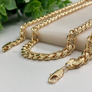 May include: A gold curb chain necklace with a lobster clasp closure. The chain is thick and has a shiny finish.