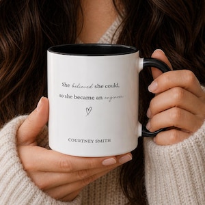 May include: White ceramic mug with a black interior and handle. The mug features the text "She believed she could, so she became an engineer" with a heart symbol and the name "COURTNEY SMITH".