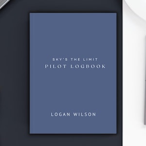 May include: A blue pilot logbook with the text "SKY'S THE LIMIT PILOT LOGBOOK" and "LOGAN WILSON" printed in white.
