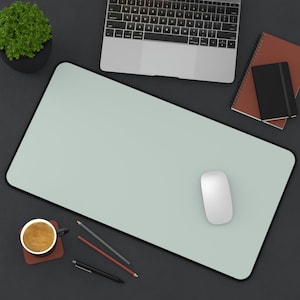 May include: A light green desk mat with a white computer mouse on top. A laptop computer, a cup of coffee, pencils, and a notebook are also on the desk.
