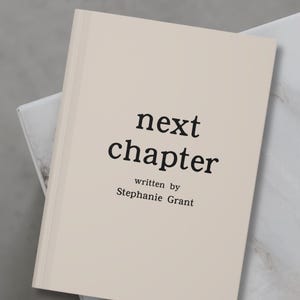 May include: A beige book with the text "next chapter" written in black font. The author's name, "Stephanie Grant", is written in smaller black font below the title.