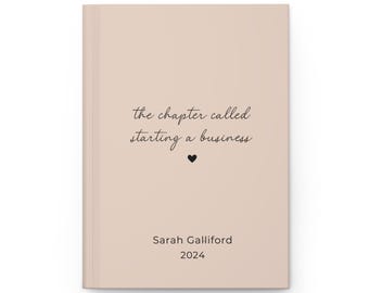May include: A light pink notebook with the text "the chapter called starting a business" and a small black heart. The notebook also has the text "Sarah Galliford 2024".