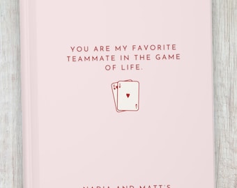 May include: A pink notebook with the text "YOU ARE MY FAVORITE TEAMMATE IN THE GAME OF LIFE." and a drawing of three playing cards. The text "NADIA AND MATT'S GAME NIGHT SCORES" is at the bottom of the notebook.