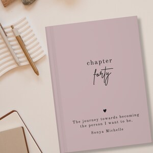 Peut inclure: Un journal de couleur rose poussiéreux avec le texte "chapter forty" et la citation "The journey towards becoming the person I want to be. Sonya Michelle" imprimée sur la couverture.