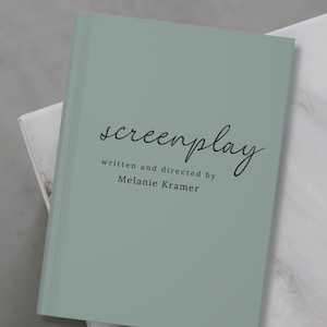 May include: A light green book with the word "screenplay" written in cursive on the front cover. The text "written and directed by Melanie Kramer" is printed below the title.