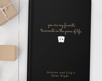 May include: A black journal with gold lettering that reads "you are my favorite teammate in the game of life."  Two playing cards are pictured above the text. The bottom of the journal reads "Jackson and Lily's Game Night".