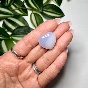 May include: A heart-shaped, polished, light blue and white agate crystal. The crystal is smooth and has a translucent appearance.