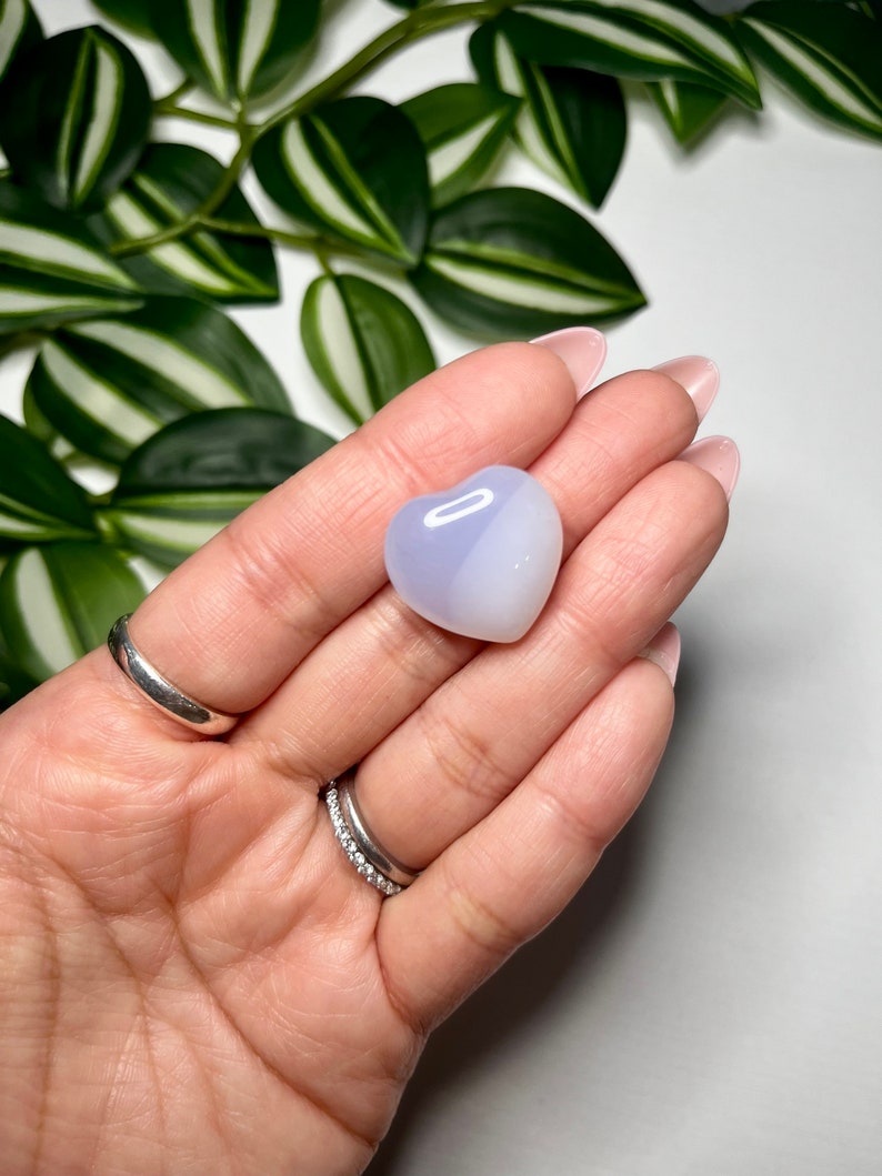 May include: A heart-shaped, polished, light blue and white agate crystal. The crystal is smooth and has a translucent appearance.