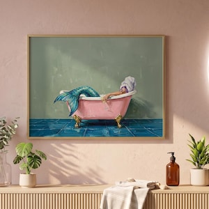 Puede incluir: Una impresión de arte de pared enmarcada que presenta una pintura de una sirena con una cola azul brillante relajándose en una bañera rosa con patas de garra. La sirena lleva una toalla blanca en la cabeza. La escena se sitúa contra una pared verde salvia y un suelo de baldosas azules.