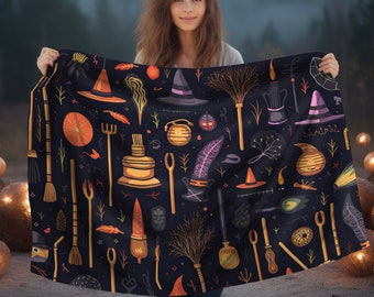 May include: A black fabric tapestry with a repeating pattern of Halloween-themed illustrations. The illustrations include witches' hats, broomsticks, cauldrons, and other magical objects. The tapestry is held by a person in front of a blurry background of trees.